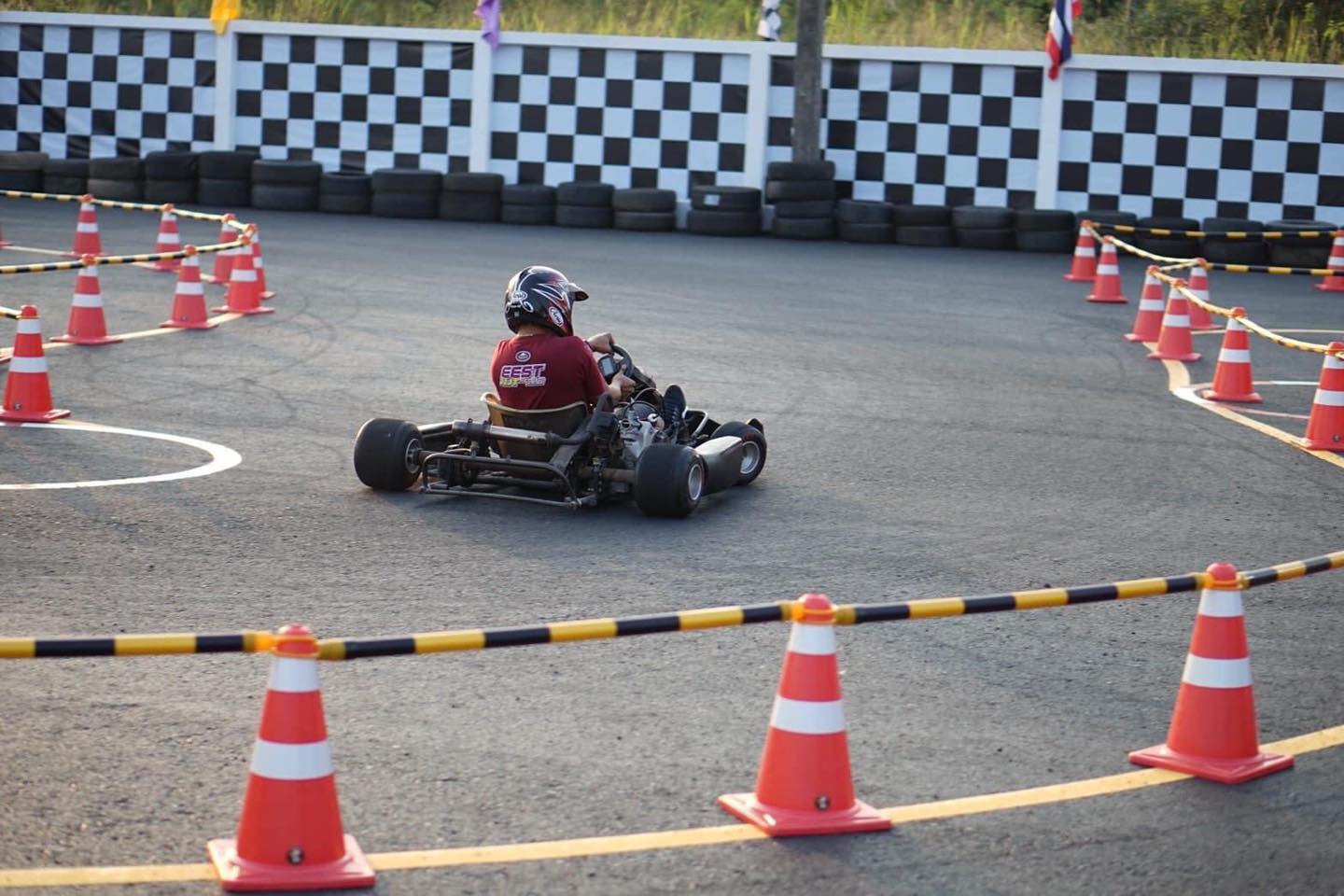 คนขับสวมหมวกกันน็อคขับโกคาร์ทผ่านแนวกรวยบนสนามฝึกซ้อม / A helmeted driver on a go-kart between the cones on the practice track