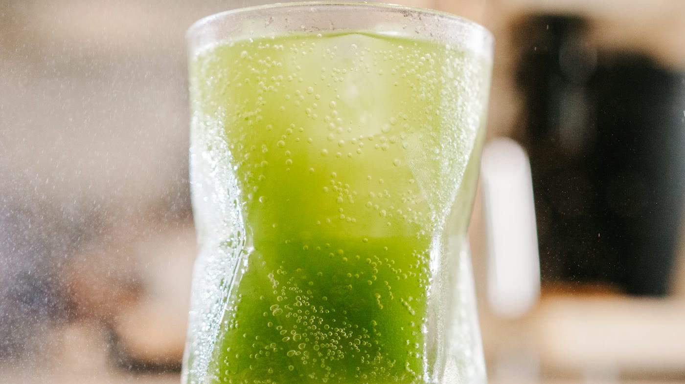 โซดาชาเขียวสีเขียวสดในแก้วใส เห็นฟองซ่าชัดเจน (ภาพประกอบ) / A bright green tea soda in a clear glass with visible carbonation (illustrative stock image)